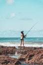 Fisherman woman with fishing rod on the rocks fishing on the beach