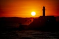 Silhouette of a lighthouse against a beautiful and dramatic orange sunset