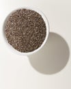 Chia Seed. Grains in a bowl. Shadow over white table.