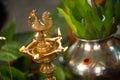 Samai oil lamp next to metal kalasha (metal pot) with leaves