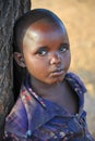 Samburu, Kenya - August 2014: Portrait of a shy young African child leaning against a tree trunk