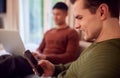 Same Sex Male Couple Sitting On Sofa At Home Using Mobile Phone And Laptop Royalty Free Stock Photo