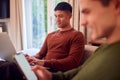 Same Sex Male Couple Sitting On Sofa At Home Using Mobile Phone And Laptop Royalty Free Stock Photo