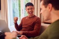 Same Sex Male Couple On Sofa At Home Using Mobile Phone And Laptop Watching Sports And Celebrating Royalty Free Stock Photo