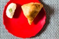 Samosa, peda barfi on red plate and woven mat, typical indian snack breakfast