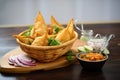 samosas in a basket with a side of sliced onions