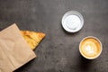 Samsa in paper envelope and cappuccino in paper cup on gray background top view