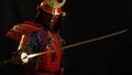A samurai man in a beautiful red armor, helmet and red defensive mask of a demon pulls out a sword from its scabbards on