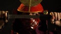 A samurai man in beautiful red armor and a mask pulls out of its scabbards katana sword