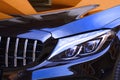 Close up headlight with colorful reflection of building and blue sky on bonnet surface of modern black car