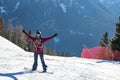 Snowboarder with arms outstretched standing on snowy mountain slope on sunny day