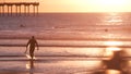 People surfing, pier on piles at sunset. Surfer in ocean water waves, California