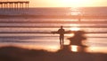 People surfing, pier on piles at sunset. Surfer in ocean water waves, California