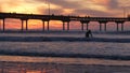 People surfing, pier on piles at sunset. Surfer in ocean water waves, California