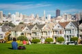 View on the Painted Ladies Victorian houses of San Francisco with cityscape and skyline in the background on a blue sky. People