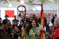 Native American two spirit person holds a traditional Grand Entry eagle staff and rainbow flag at powwow, San Francisco