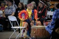 Native Americans dressed in intricate and colorful traditional outfits sing a song and drum at a powwow in San Francisco