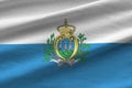 San Marino flag with big folds waving close up under the studio light indoors. The official symbols and colors in banner