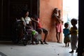 Beggar on wheelchair with other beggars and children having fun at church door gate portal