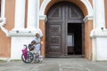 Lady, Blind Man beside disabled Beggar in wheelchair at Church yard Gate Portal
