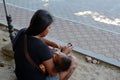 Woman cuddling sleeping little son clicking a mobile phone seated on church yard sidewalk