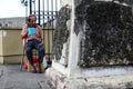 Blind old male beggar seeking alms at churchyard gate portal