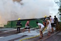 Firemen and volunteers on rooftop put out fire using fire hose during house fire that gutted interior shanty houses