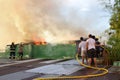 Firemen and volunteers on rooftop put out fire using fire hose during house fire that gutted interior shanty houses