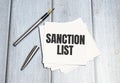 SANCTION LIST text on white paper with pen on wooden background