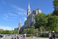 Esplanade alongside the Sanctuary of Our Lady of Lourdes, with the imposing spire of the Upper Basilica rising above the grotto