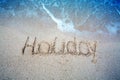 Holiday written in the sand on the beach waves in the background Royalty Free Stock Photo