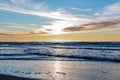 Sand beach with endless horizon and foamy waves under the bright sundown with yellow colors and clouds above the sea Royalty Free Stock Photo