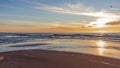 Sand beach with endless horizon and foamy waves under the bright sundown with yellow colors and clouds above the sea