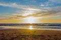 Sand beach with endless horizon and foamy waves under the bright sundown with yellow colors and clouds above the sea Royalty Free Stock Photo