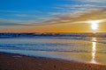 Sand beach with endless horizon and foamy waves under the bright sundown with yellow colors and clouds above the sea Royalty Free Stock Photo