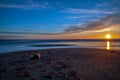 Sand beach with endless horizon and foamy waves under the bright sundown with yellow colors and clouds above the sea Royalty Free Stock Photo