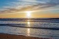 Sand beach with endless horizon and foamy waves under the bright sundown with yellow colors and clouds above the sea