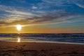 Sand beach with endless horizon and foamy waves under the bright sundown with yellow colors and clouds above the sea Royalty Free Stock Photo