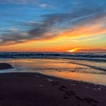 Sand beach with endless horizon and foamy waves under the bright sundown with yellow colors and clouds above the sea Royalty Free Stock Photo