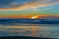 Sand beach with endless horizon and foamy waves under the bright sundown with yellow colors and clouds above the sea Royalty Free Stock Photo