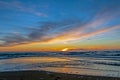 Sand beach with endless horizon and foamy waves under the bright sundown with yellow colors and clouds above the sea Royalty Free Stock Photo