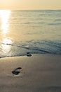 Sand beach, wave and footsteps at sunset Royalty Free Stock Photo