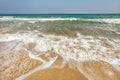 Sand on the beach wet from small waves; azure sea ad clear sky in background