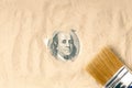 Sand cleaning brush, one hundred dollars dug out of the sand. The president`s portrait peeps out of quicksand Royalty Free Stock Photo