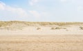 Sand dunes on a seaside of North Sea beach with some grass and fence. Cloudy blue sky and marine style landscape. Royalty Free Stock Photo