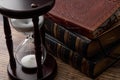 Sand flowing in vintage hourglass next to stack of ragged books concept for vanishing of quality reading time, diminishing Royalty Free Stock Photo
