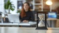 A Sand Glass Measuring Time on a Desk While a Woman Concentrates on Her Computer Work