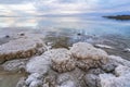 Sand and stones covered with crystalline salt on shore of Dead Sea, clear water background - typical morning scenery at Royalty Free Stock Photo