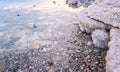 Sand and stones covered with crystalline salt on shore of Dead Sea, clear water near - typical scenery at Ein Bokek beach, Israel Royalty Free Stock Photo