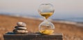 Sandglass on a wooden board with three stones in the form of a pyramid, a modern hourglass on a beach with golden sand against the